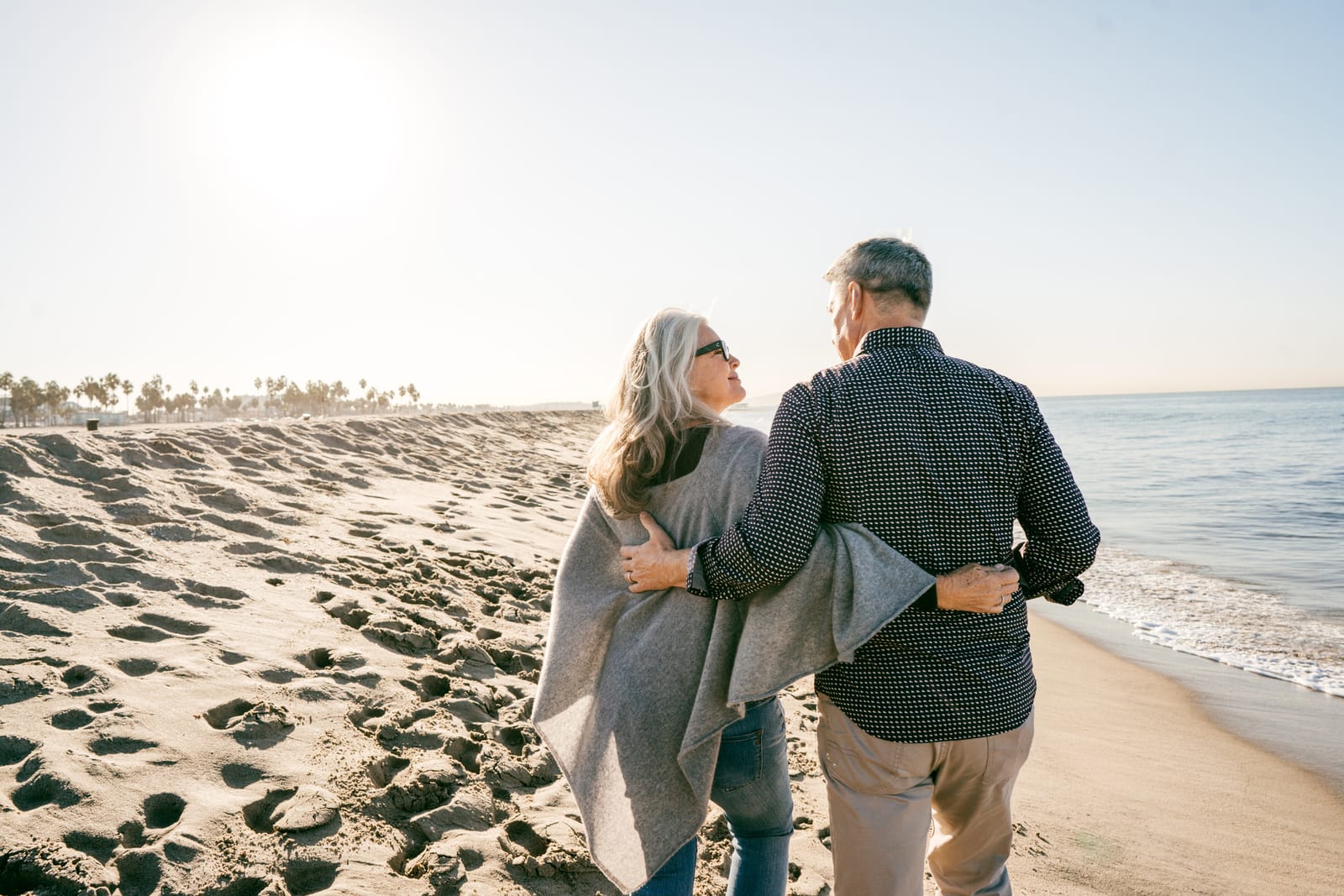 A retired couple walking arm in arm along a sunny beach