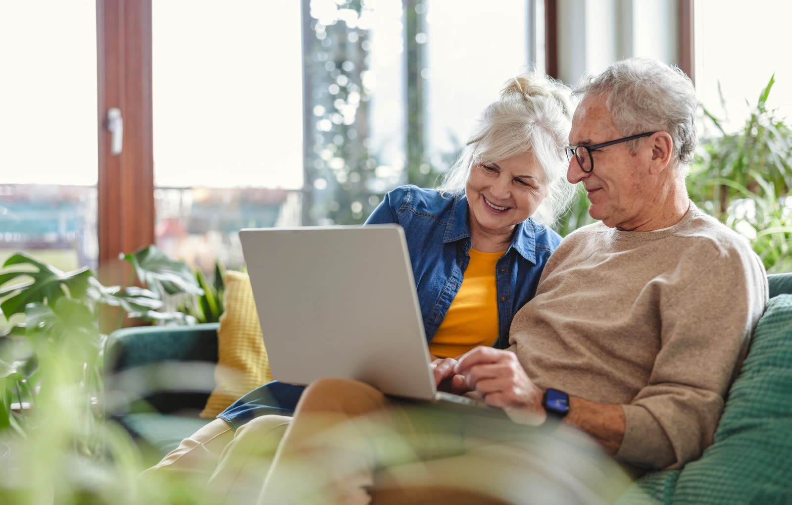 Older couple smiling on a sofa while reviewing something together on a laptop